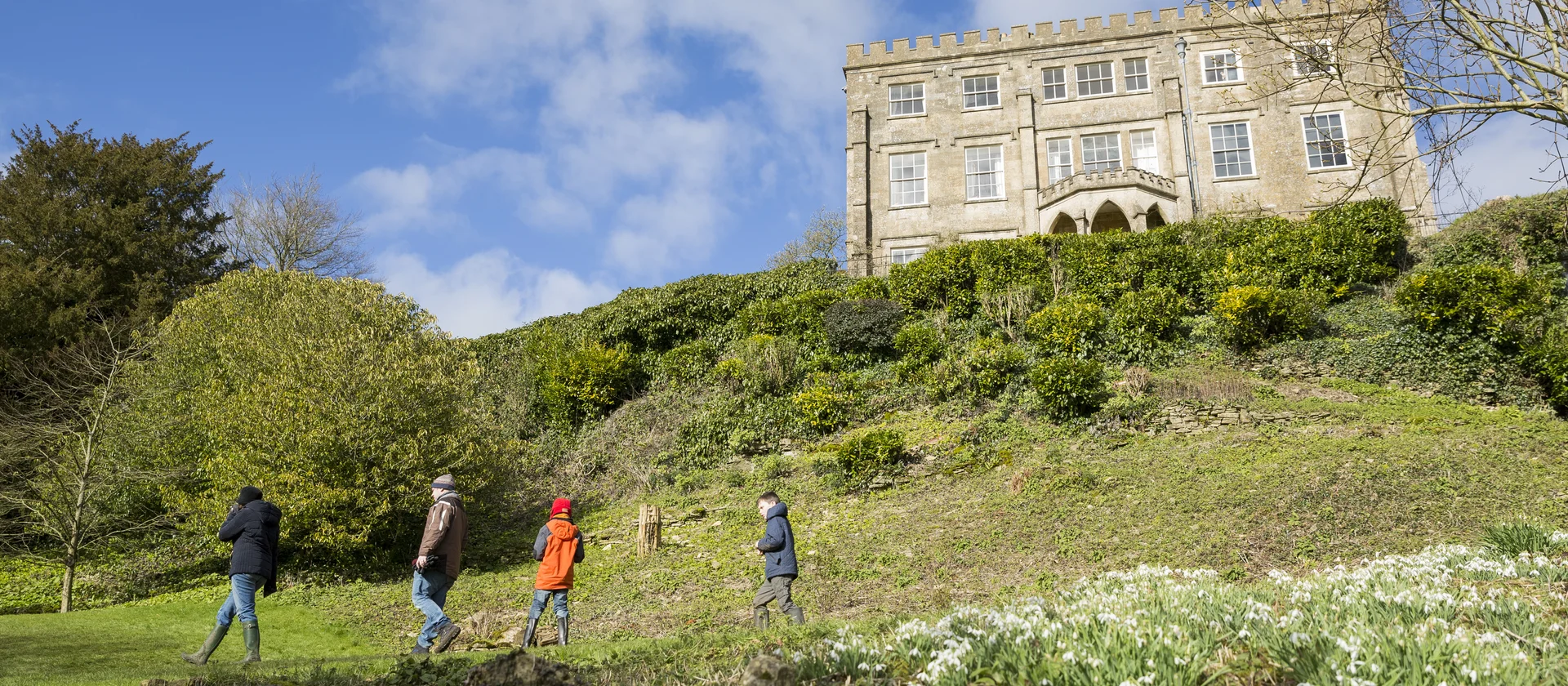People walking in gardens in front of a grand English stately home