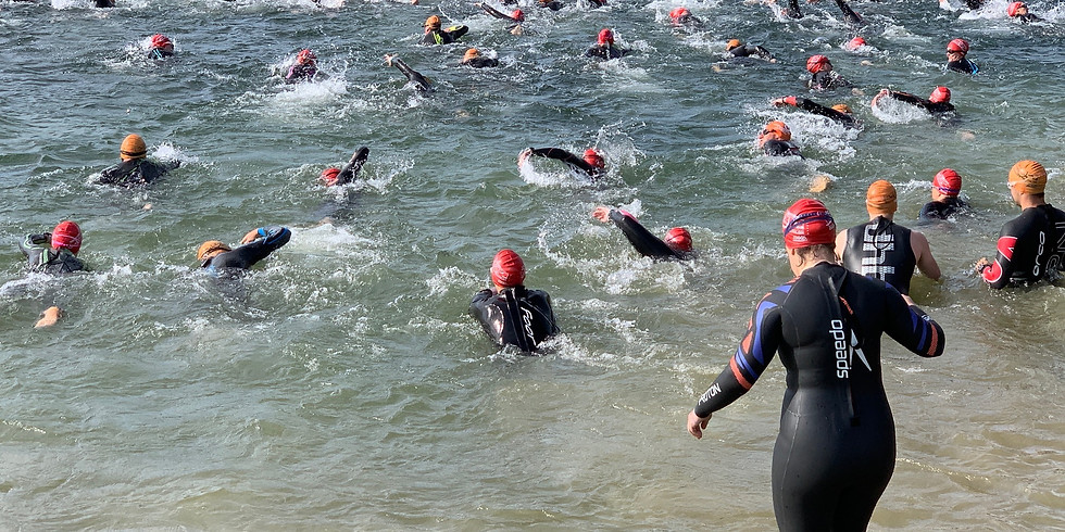 Group of people in wet suits and swimming hats entering a lake to race
