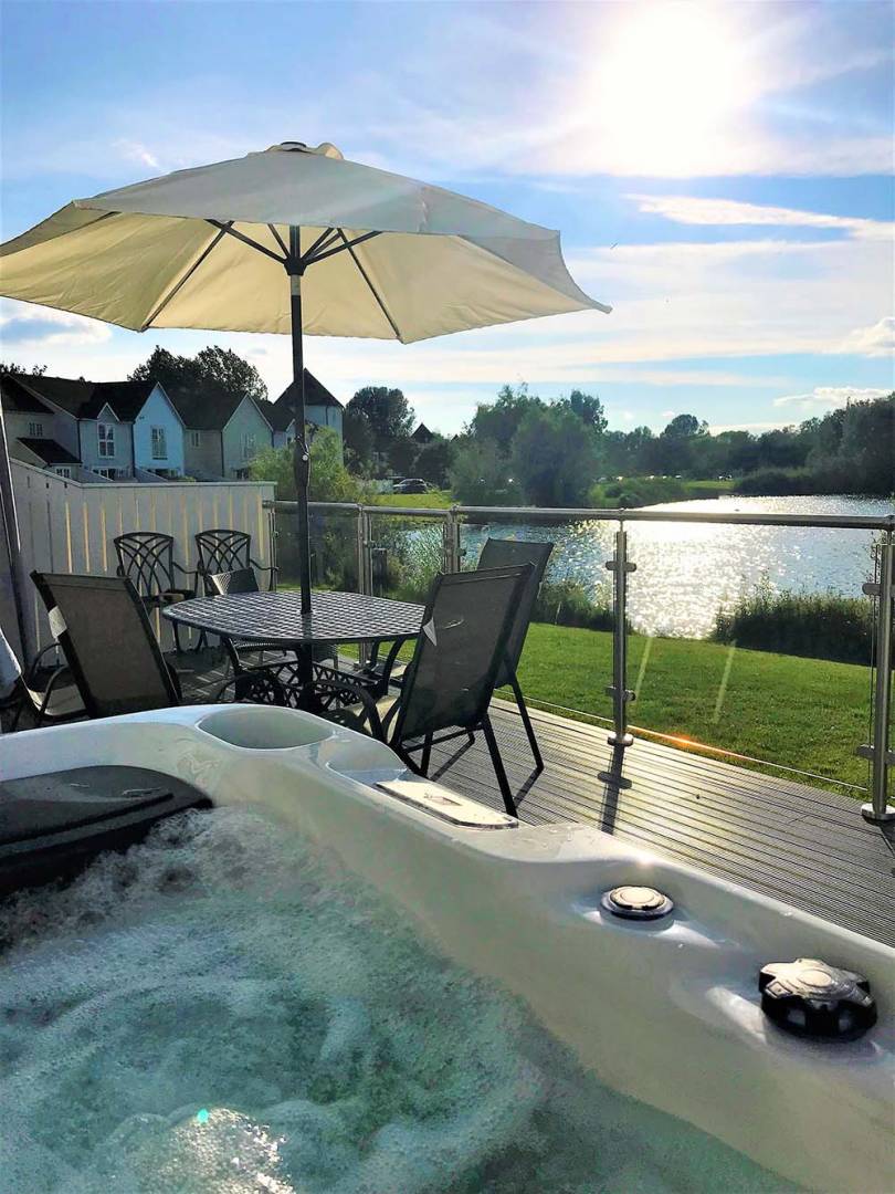Hot tub on decking next to outdoor dining table with umbrella