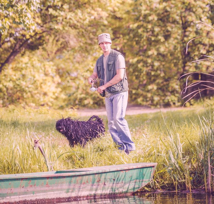man standing on the bank of a river fishing with his dog