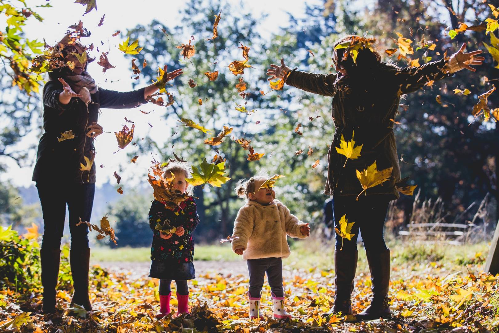 Family chasing fallen leaves at Westonbirt Arboretum during autumn half term in the Cotswolds